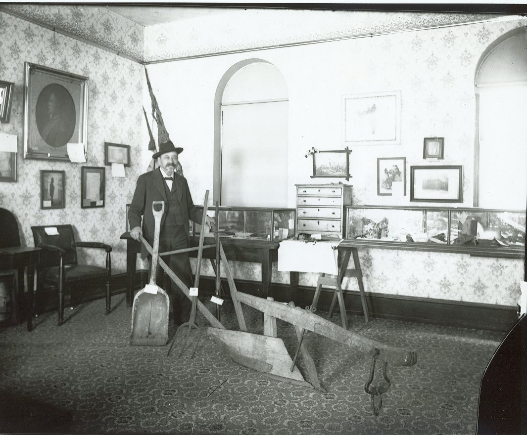 Photo of William E. Miller, Congressional Medal of Honor recipient and President of the Hamilton Library Association stands with museum exhibits in one of the rooms of the Hamilton Library (now CCHS).
