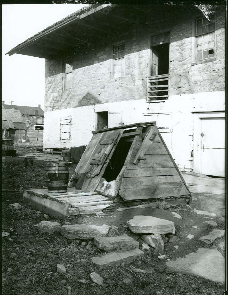 The well at the old distillery, seen with its bucket and chain, was 96 feet deep. Taken c. 1900 by A. A. Line.