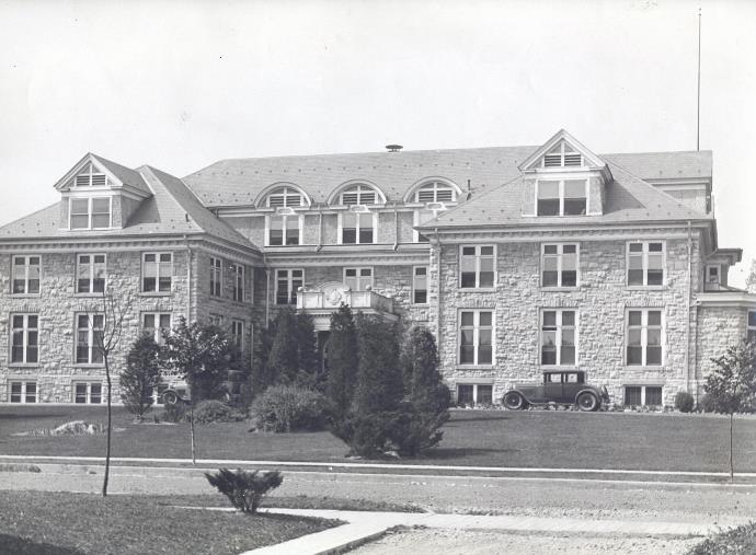 Photo of the front view of the Carlisle Hospital with two automobiles near entrance 