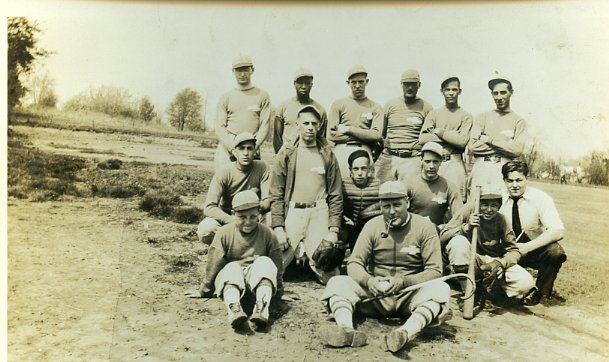 Photo of Posed  outdoor snapshot of  a baseball team with everyone in uniform except a man in white shirt and tie.