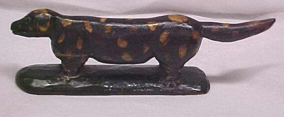 Woodcarving of a standing dog painted brown with yellow spots atop a dark green base.