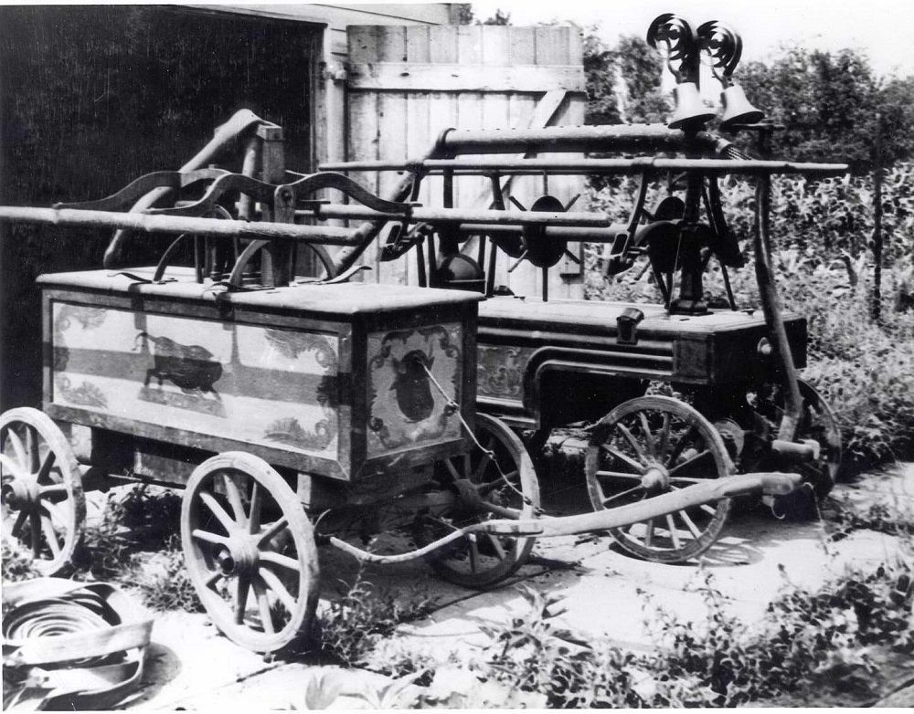 Image of two old horsedrawn firewagons sitting outside storage shed.