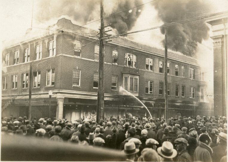 The Kronenberg building on fire, with a large crowd watching the firemen spraying water on the building.