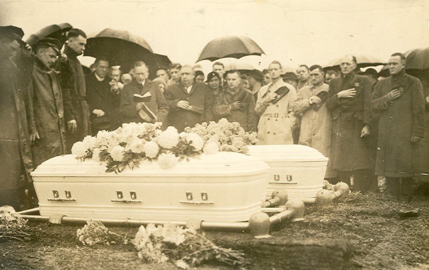 Outdoor B&W photo of a men and women standing around coffins in Westminster Cemetery near Carlisle, PA. Two coffins are visible, and a third is probably hidden behind one.